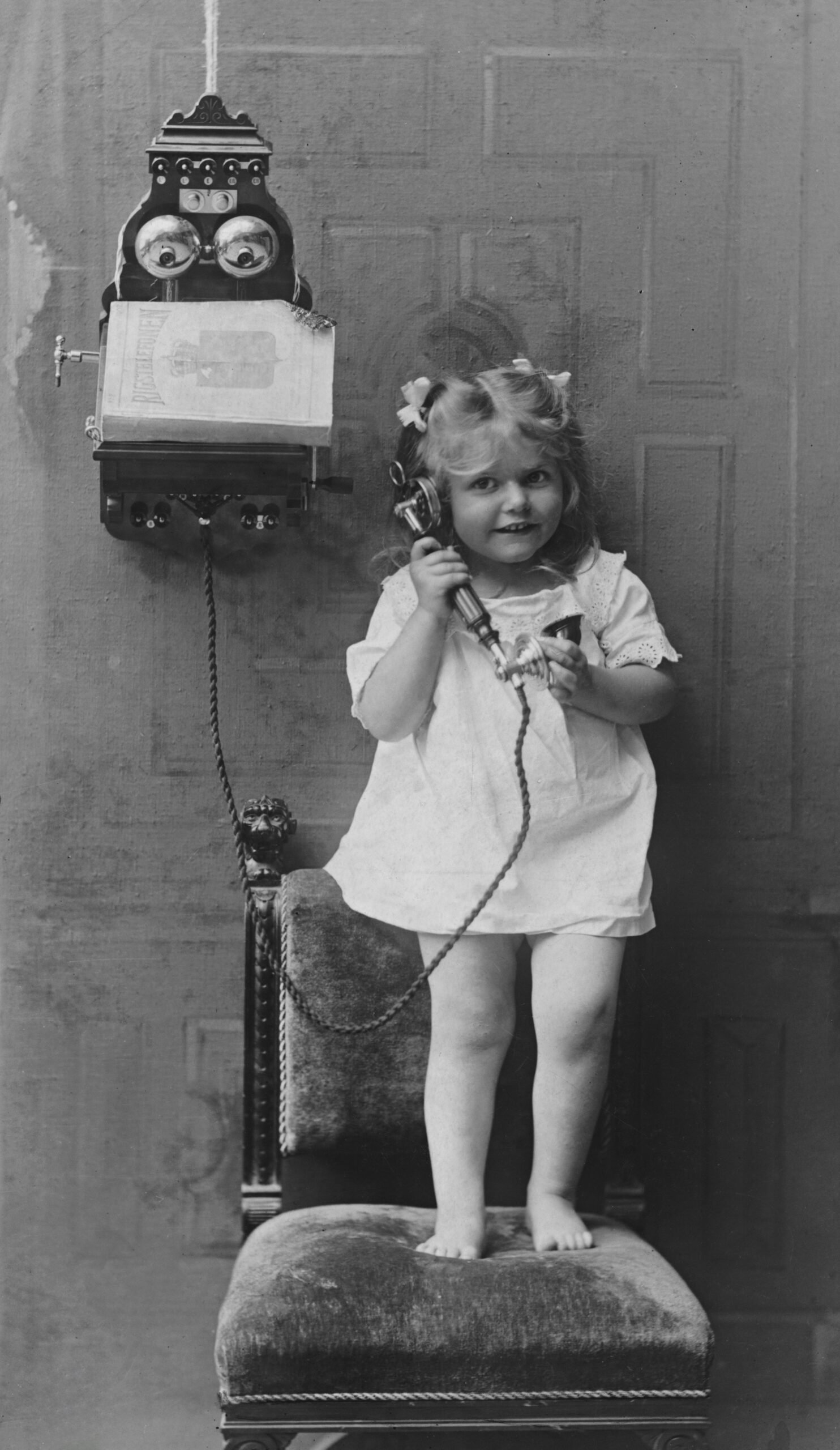 A little girl stands on a chair holding a telephone to her ear